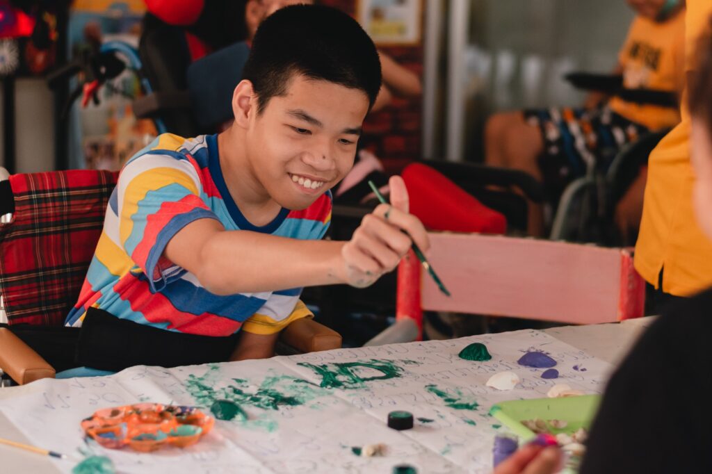 Handicapped teenager boy on wheelchair with happy face doing art work with friends.
